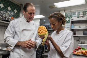 Chef in kitchen teaching CASA culinary school student to cut fruit